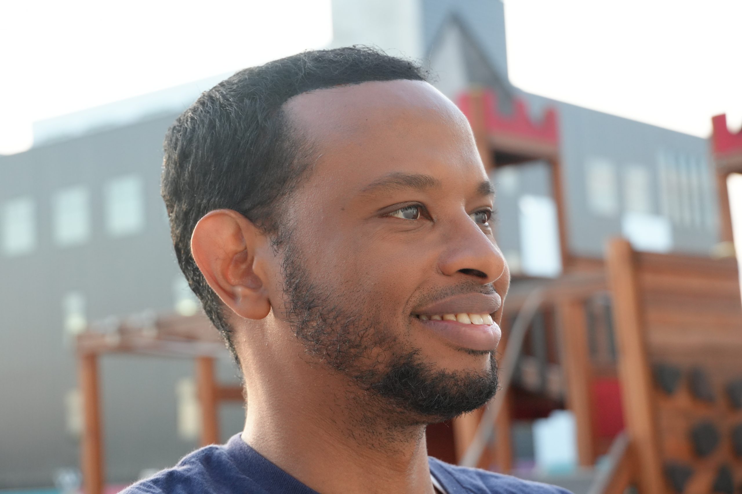 Abdihakim Ibrahim in profile at golden hour, smiling toward a neighborhood playground